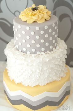 a three tiered cake with yellow flowers and gray polka dots on the bottom layer