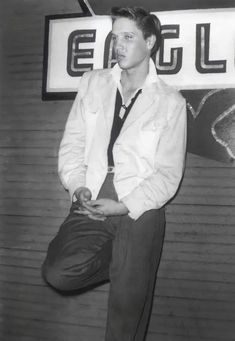 a man standing in front of a sign wearing a tie and suit coat with his hands in his pockets