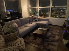 a living room filled with furniture next to a window covered in night time lights and windows