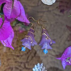 purple flowers and blue glass beads are hanging from gold plated earwires on a table