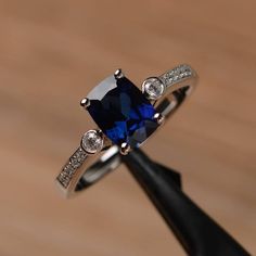 an engagement ring with a blue stone surrounded by white diamonds on top of a wooden table