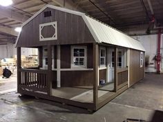 a small wooden building with a porch and windows on the roof, in a warehouse