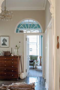 an archway leads into a living room with a dresser, chair and rug on the floor