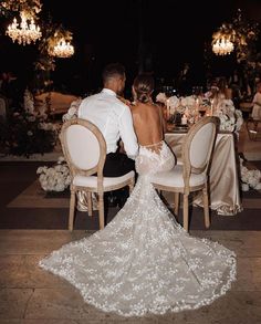 a bride and groom sitting at a table in front of chandeliers with white flowers