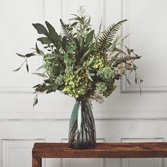 a vase filled with lots of green flowers on top of a wooden table next to a white wall