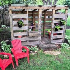 two red chairs sitting in front of a wooden structure with plants growing on it's sides