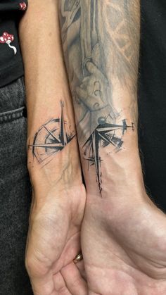 two people are holding hands with tattoos on their arms and wrist, one has a compass