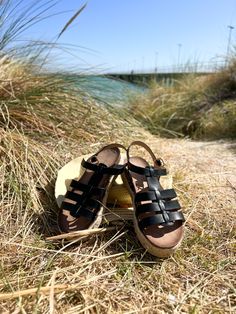 a pair of sandals sitting on top of a beach next to grass and the ocean