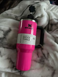 a pink travel mug sitting on top of a bed next to a black keychain