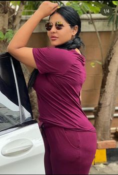 a woman standing next to a white car with her hand on the hood and wearing sunglasses