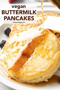 a plate topped with pancakes covered in butter and blueberries next to syrup being poured on top