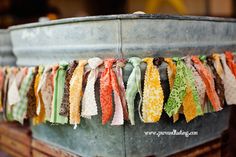 an old metal bucket filled with lots of different colored fabric pieces hanging from it's sides