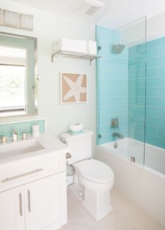 a white toilet sitting next to a bath tub under a bathroom window with blue tiles on the walls