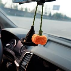 an orange and black crocheted hat hanging from the dashboard of a parked car