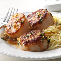 three scallops with sauce and pasta on a white plate next to a fork