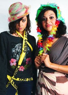 two women wearing colorful hats and scarves pose for the camera with one woman holding a flower in her hand