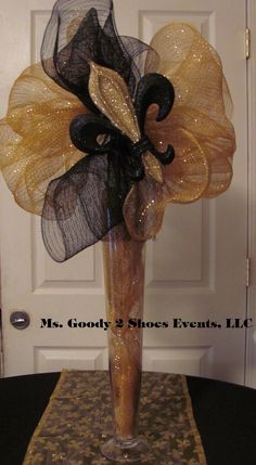 a tall vase filled with black and gold mesh flowers on top of a table next to a door