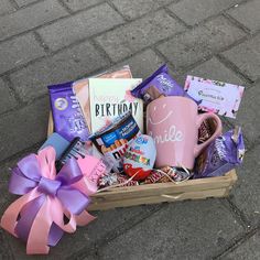 a pink coffee mug filled with lots of goodies next to a purple bow on the ground