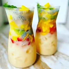 two glasses filled with fruit and veggies on top of a table