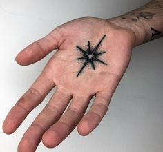 a person's hand with a small black star tattoo on the middle of it