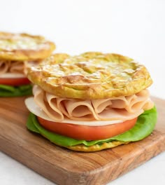 two sandwiches with ham, lettuce and tomato on a wooden cutting board next to each other