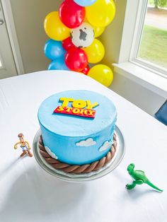 a birthday cake sitting on top of a table next to a toy dinosaur and balloon