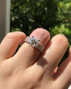 a woman's hand with a diamond ring on her finger and trees in the background