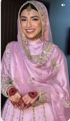 a woman in a pink dress and headpiece smiles at the camera with her hands on her chest