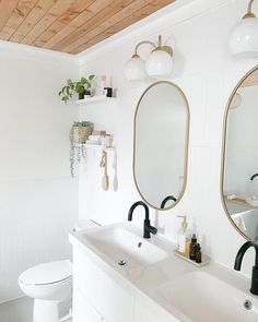 a white bathroom with two mirrors above the sink and a toilet in front of it