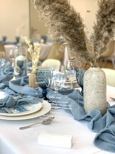 the table is set with blue linens, silverware and flowers in glass vases