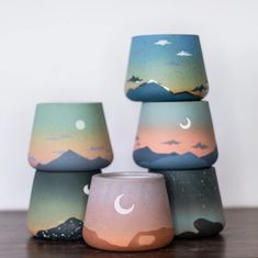 three candles sitting on top of a wooden table next to each other with mountains in the background