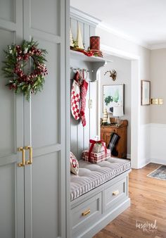 a christmas wreath is hanging on the wall next to a bench in a room with gray cabinets