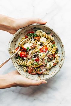 two hands holding a bowl of pasta with tomatoes, mushrooms and parmesan cheese