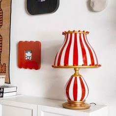 a red and white striped lamp sitting on top of a table next to a clock