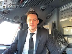 a man wearing a suit and tie sitting in the cockpit of an airplane looking at the camera