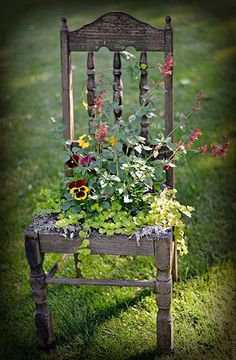 an old chair with flowers growing out of it's seat is on the grass