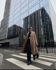 a woman walking across a cross walk in front of tall buildings with glass windows on each side