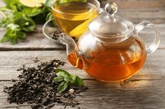 two teapots filled with different types of green tea and leaves on a wooden table