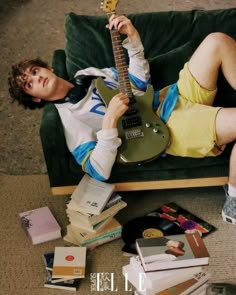 a man laying on top of a green couch with a guitar in his hand and lots of books around him