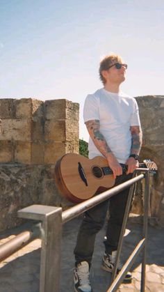 a man holding a guitar while standing next to a fence