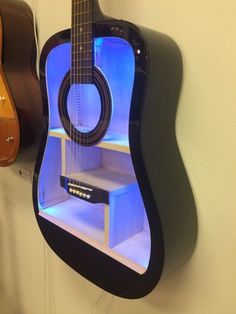 a guitar shaped shelf with a blue light on it's side and a guitar hanging from the wall