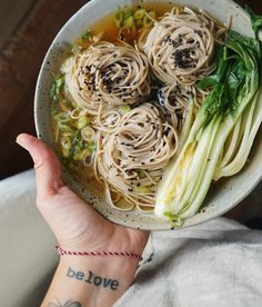 a person holding a bowl of noodles and vegetables