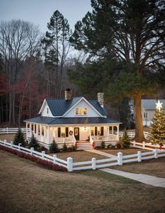 a white house with a christmas tree in the yard and lights on it's front porch