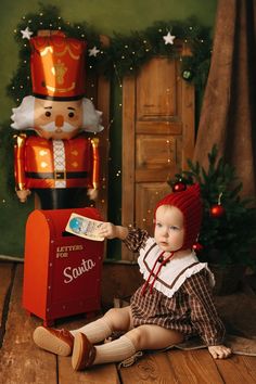 a baby sitting on the floor in front of a mailbox with a nutcracker