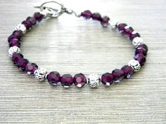 This is a beaded bracelet made of purple glass beads. Silver colored round beads add a pretty touch. The bracelet fastens with a toggle clasp. It is 8 inches long from one clasp end to the other. Unique Purple Bracelets With Round Beads, Faceted Purple Beaded Bracelets, Purple Polished Beads Bracelet, Purple Polished Bead Bracelet, Adjustable Hand-wrapped Purple Beaded Bracelet, Purple Czech Glass Beaded Bracelets, Handmade Purple Glass Bracelets, Dinosaur Earrings, Book Earrings