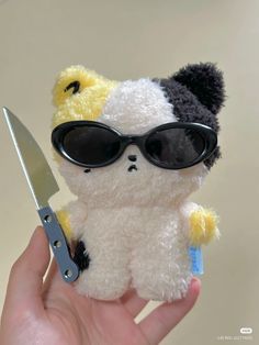 a hand holding a small stuffed animal with sunglasses on it's face and a pair of scissors in its other hand