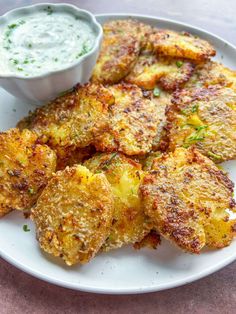 some fried food on a white plate with a small bowl of ranch dressing next to it