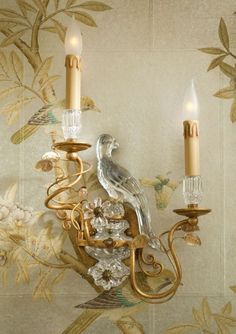 a wall light with two candles on it and a bird figurine next to it