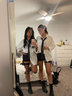 two young women standing in front of a bed looking at their cell phones while wearing short shorts and high heels