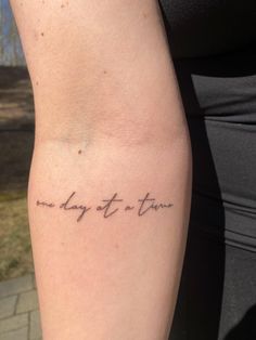 a woman's arm with the words one day at a time written on it